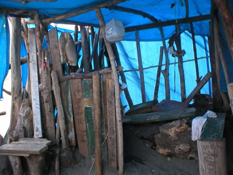 1978 Ford Bronco - Interior view of a rustic shelter made of wood and covered with a blue tarp, showing writings on planks.