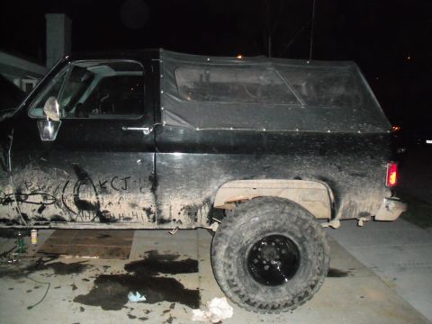1991 Ford Bronco - A muddy, graffiti-covered black SUV with a soft top is parked on a concrete surface at night.