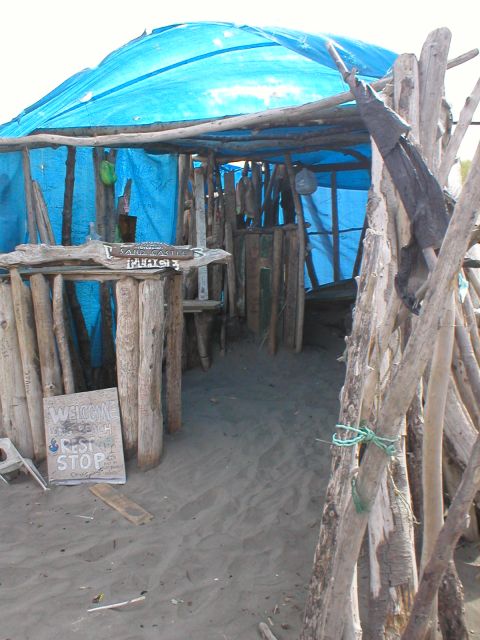1978 Ford Bronco - A rustic beach shelter constructed from driftwood and a blue tarp provides shade and a place to rest.