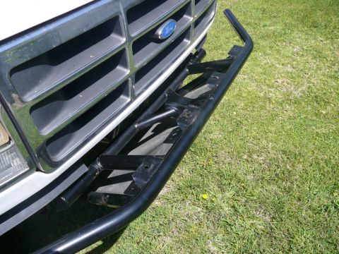 1988 Ford Bronco - Close-up of a Ford truck's front grille and aftermarket brush guard, set against a grassy background.