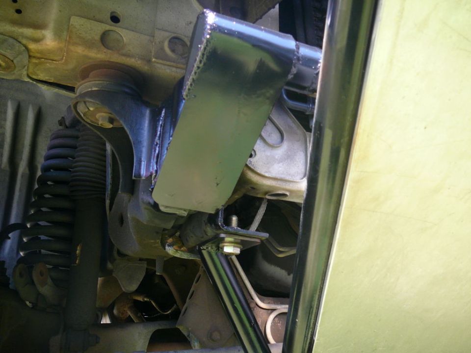 Undercarriage of a vehicle showing suspension and a black metal bracket. Light yellow body panel visible