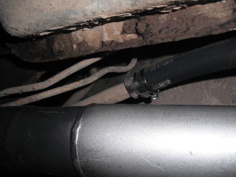 1991 Ford Bronco - A close-up view of a hose connected to a pipe, with other vehicle undercarriage components visible.