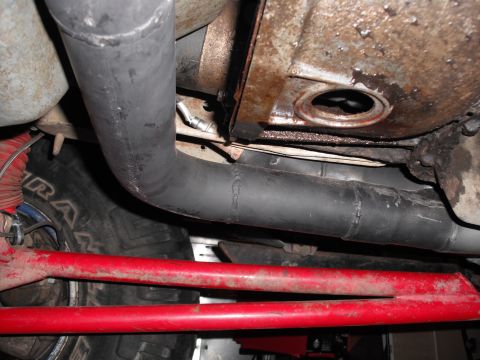 1991 Ford Bronco - Close-up view of a custom exhaust y-pipe installation, showing the underside of a vehicle with red suspension parts and a tire.