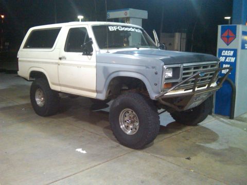 1986 Ford Bronco - A modified Ford Bronco sits at a gas station with its hood and fender unpainted.