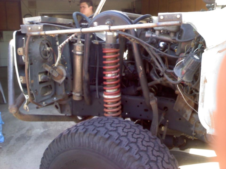 Front tire and disassembled engine bay of a white vehicle with red coil springs