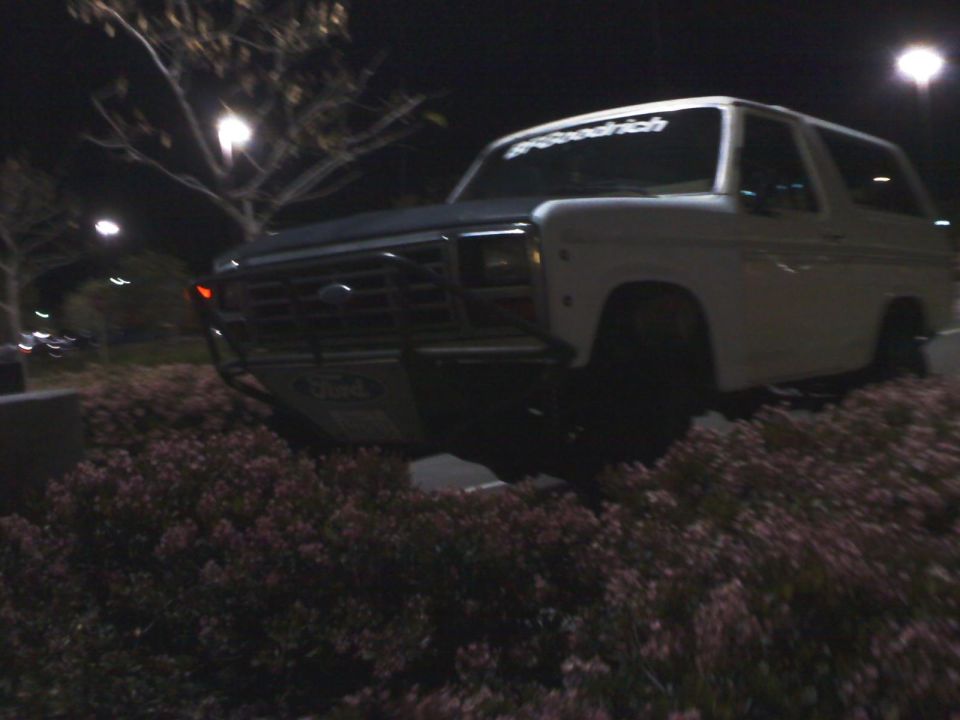 White Ford Bronco with a brush guard parked at night. BFGoodrich sticker on windshield