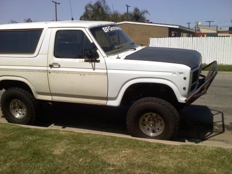 1986 Ford Bronco - This white Ford Bronco, likely from the early 1980s, has a custom front bumper and a matte black hood.