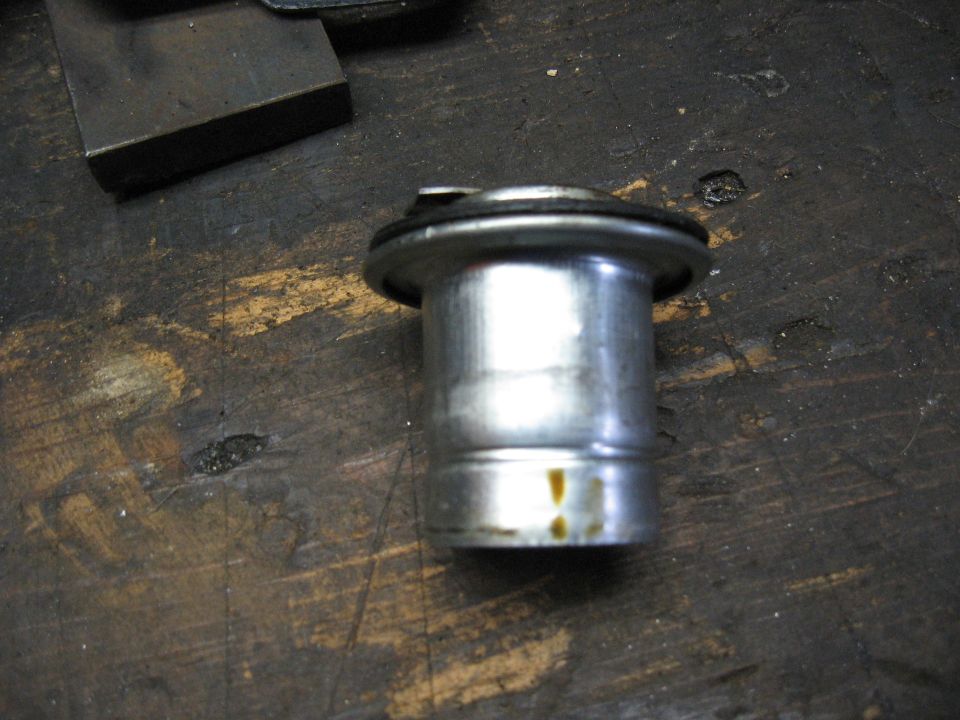 Metal automotive part with a rubber seal, resting on a dark wooden surface