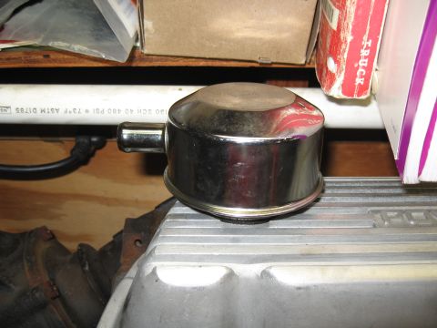 1994 Ford Bronco - A chrome oil cap is positioned on a silver engine valve cover, with a white pipe and some boxes in the background.