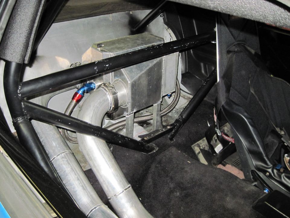 Interior view of a car's passenger side, showing a roll cage, fuel cell, and exhaust pipes