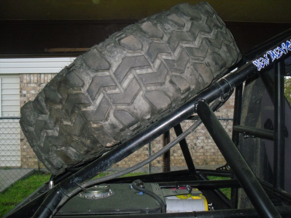 Spare tire mounted on roll cage of an off-road vehicle. Some text is visible on the cage