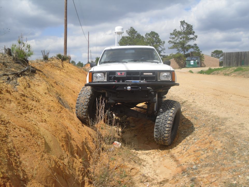 White Toyota pickup truck with lifted suspension and large tires driving on a dirt path with a steep embankment