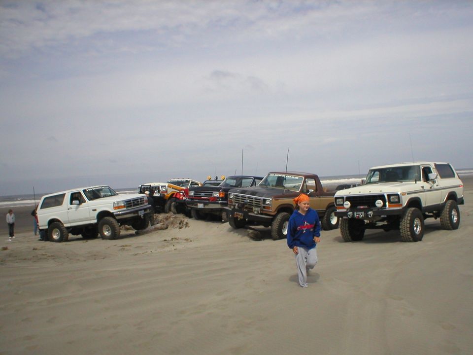 White 1978 Ford Bronco parked on a sandy beach with other vehicles