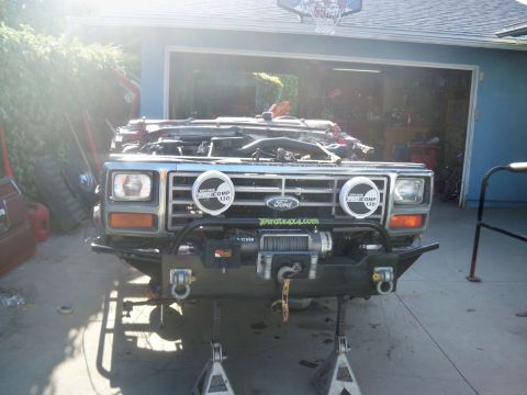 1985 Ford Bronco - Front view of a 1985 Ford Bronco undergoing repairs, an open hood, winch, and auxiliary lighting.