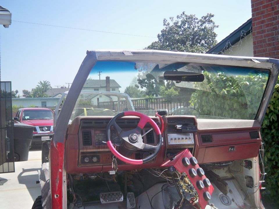 Interior of a red vehicle with dashboard removed, custom steering wheel, and exposed wiring