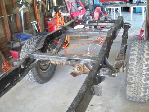 1985 Ford Bronco - Frame and suspension components of a vehicle in a garage setting, possibly undergoing restoration.