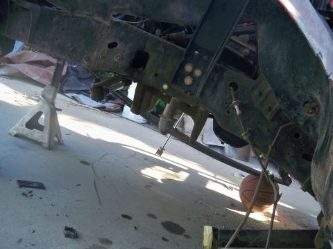 1985 Ford Bronco - The underside of a vehicle is supported by jack stands, with a basketball visible near the suspension components.