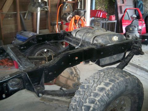 1985 Ford Bronco - The chassis of a vehicle is shown with its fuel tank and suspension parts, undergoing work in a garage.