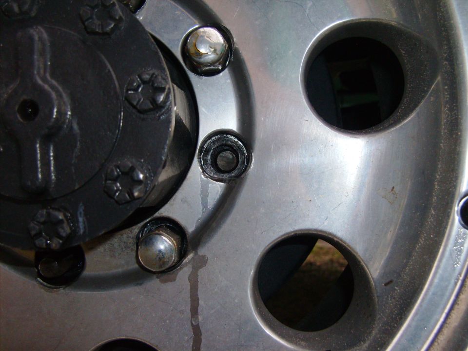 Close-up of polished wheel center with chrome lug nuts, missing lug and dark locking hub