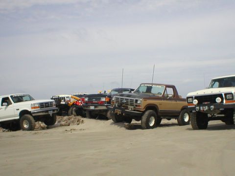 1978 Ford Bronco - Group of Ford Broncos and trucks gathered on a beach, likely for an off-road event.