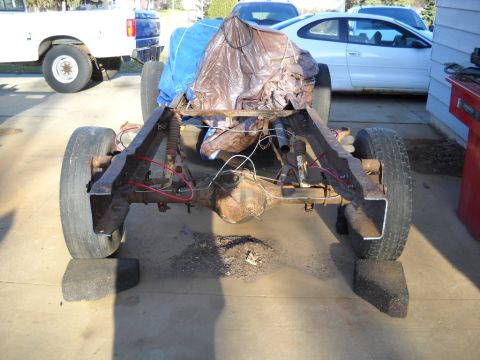 1954 Ford F-100 - Rear view of a truck chassis with a tarp-covered load, other vehicles visible in the background.