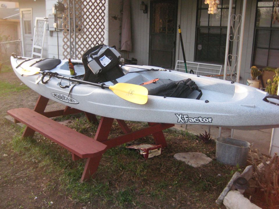 Gray kayak with yellow paddle and black bag on a red picnic table