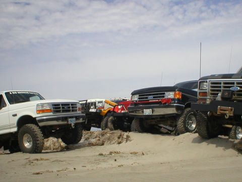 1978 Ford Bronco - A group of off-road vehicles are gathered on a sandy terrain, with a clear sky overhead.