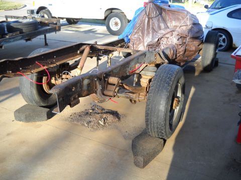 1954 Ford F-100 - A heavily rusted truck chassis is supported by blocks, with other vehicles visible in the background.