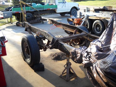1954 Ford F-100 - A disassembled truck chassis is supported by jack stands, with other vehicles and equipment visible in the background.
