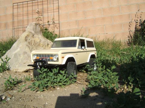 1988 Ford Bronco - A remote-controlled toy car resembling a vintage SUV is positioned outdoors amidst foliage and dirt.