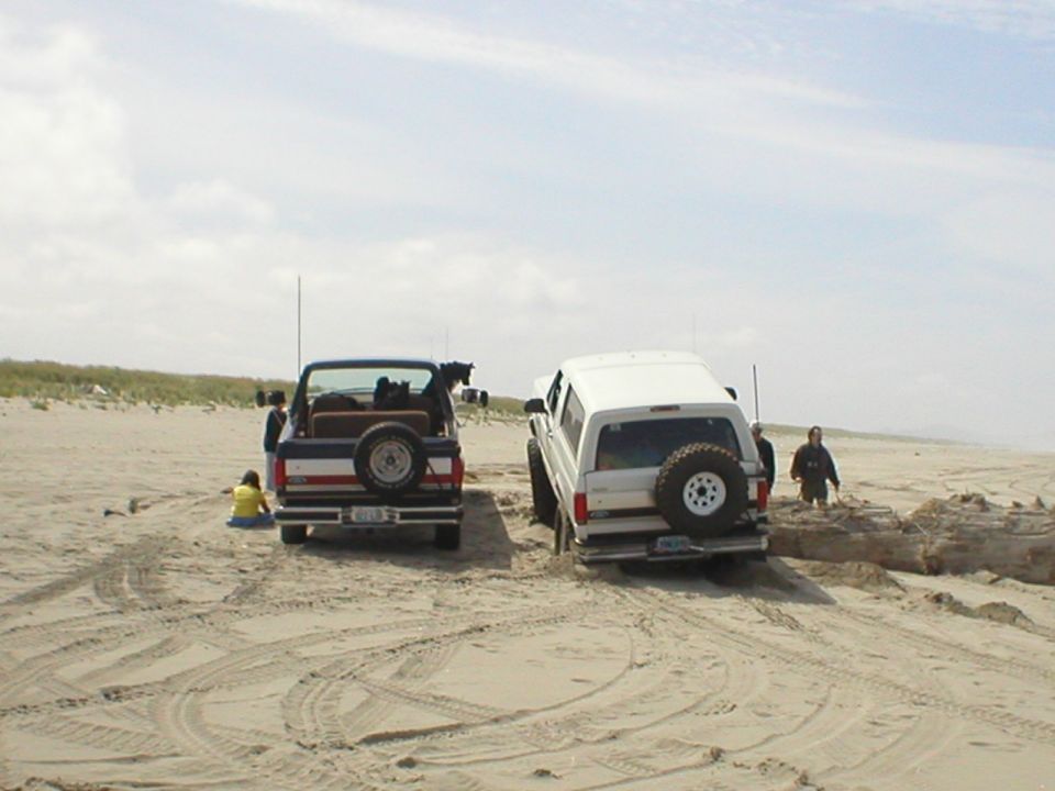 Two SUVs on a sandy beach, one blue and red, one white