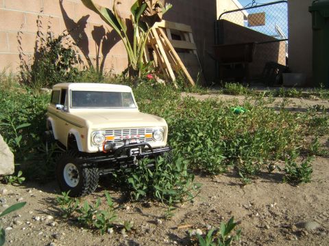 1988 Ford Bronco - A remote-controlled toy truck resembling an early Ford Bronco sits in a patch of weeds and dirt.