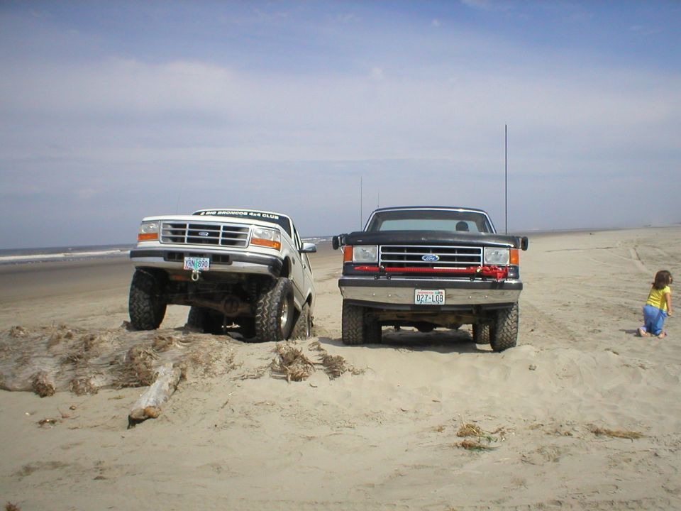 White Ford truck stuck in sand, black Ford truck parked nearby on beach
