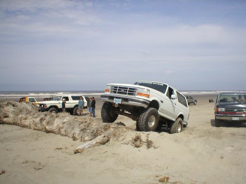1978 Ford Bronco - Several 4x4 vehicles are gathered on a sandy beach, with one Bronco navigating a dirt mound.