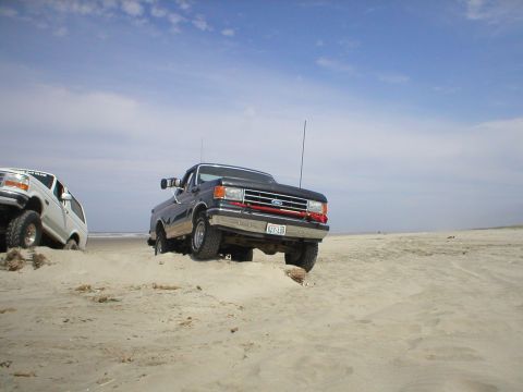 1978 Ford Bronco - Two trucks are on a sandy beach under a cloudy sky.
