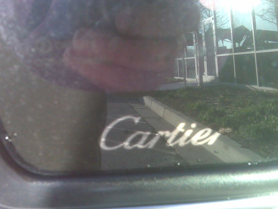 Cartier text reflected on a car window, with a building in the background