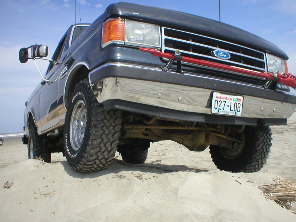 Front view of dark blue Ford truck with chrome bumper and off-road tires on sand