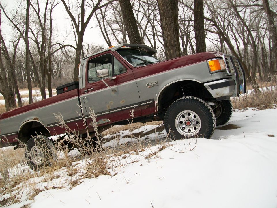 1988 Ford F-150 pickup truck with two-tone paint and a brush guard, parked in a snowy wooded area