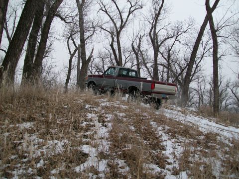 1988 Ford F-150 - A Ford F-150 pickup truck drives up a snowy incline surrounded by bare trees.