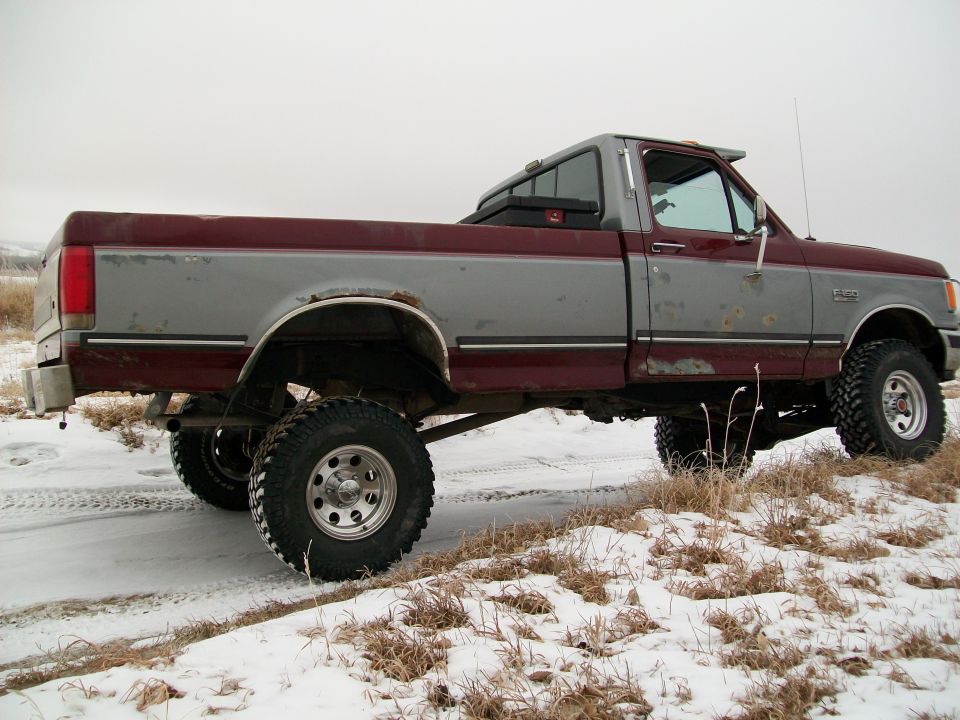 1988 Ford F-150 pickup truck with two-tone paint and lifted suspension parked on a snowy dirt road