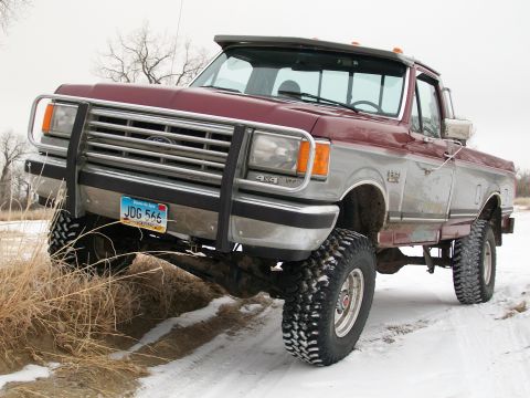 1988 Ford F-150 - This lifted Ford F-Series truck is shown on a snowy, off-road path with a two-tone paint scheme.