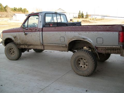 1988 Ford F-150 - This lifted pickup truck is covered in mud, suggesting recent off-road use.