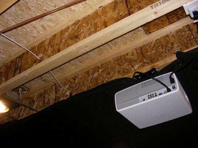 Ceiling-mounted projector pointing up at exposed OSB floor joists