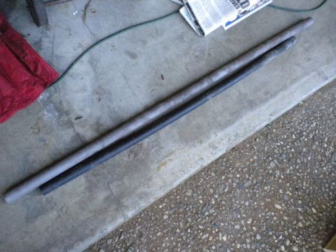 1989 Ford Bronco - Two metal bars are laid out on a concrete floor, possibly for a vehicle repair or modification.
