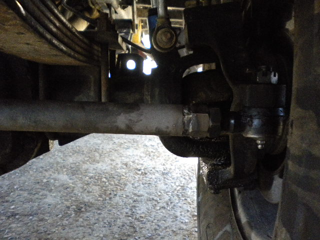Underside close-up of a solid front axle knuckle, steering linkage and leaf spring