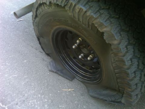 1986 Ford Bronco - The tire is completely flat and damaged, resting on the rim.