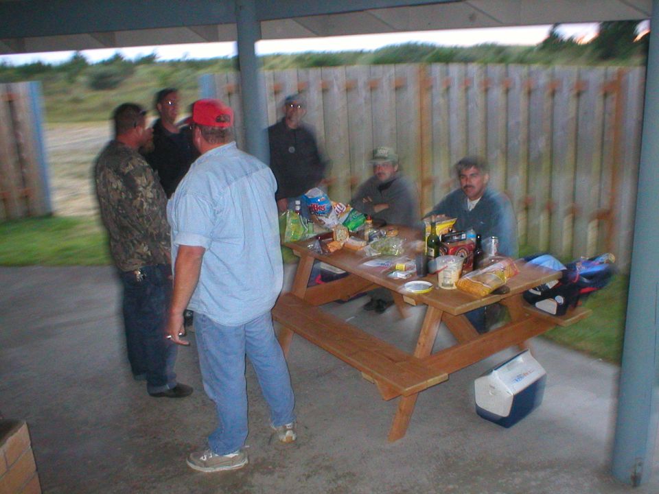 Group of men gathered around a picnic table with food and drinks
