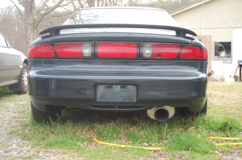 1996 Ford Probe - Rear view of a dark coupe with a spoiler and aftermarket exhaust, parked next to another vehicle.
