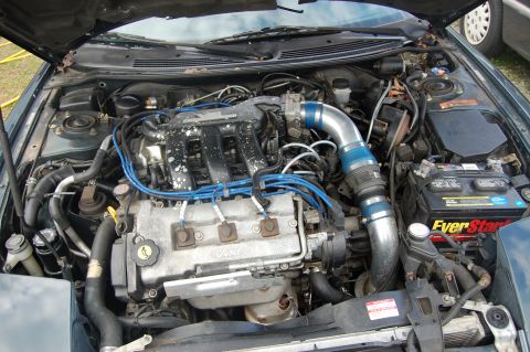 1996 Ford Probe - The engine bay of a Ford vehicle is shown with various components and blue spark plug wires.