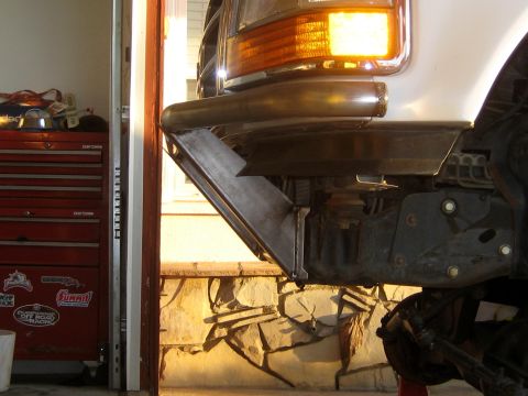 1996 Ford Bronco - Close-up view of the front bumper and suspension system of a white vehicle, with an orange turn signal illuminated.